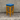 Wooden bar stool with a blue cushioned seat against a concrete wall.