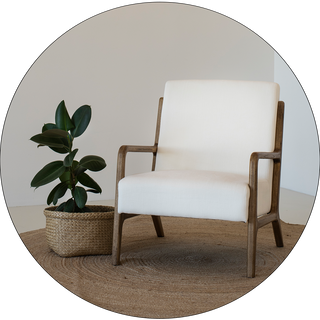 Simple arm chair with white seat and back cushions next to a houseplant