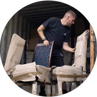 Man moving dark wooden chairs into a shipping container