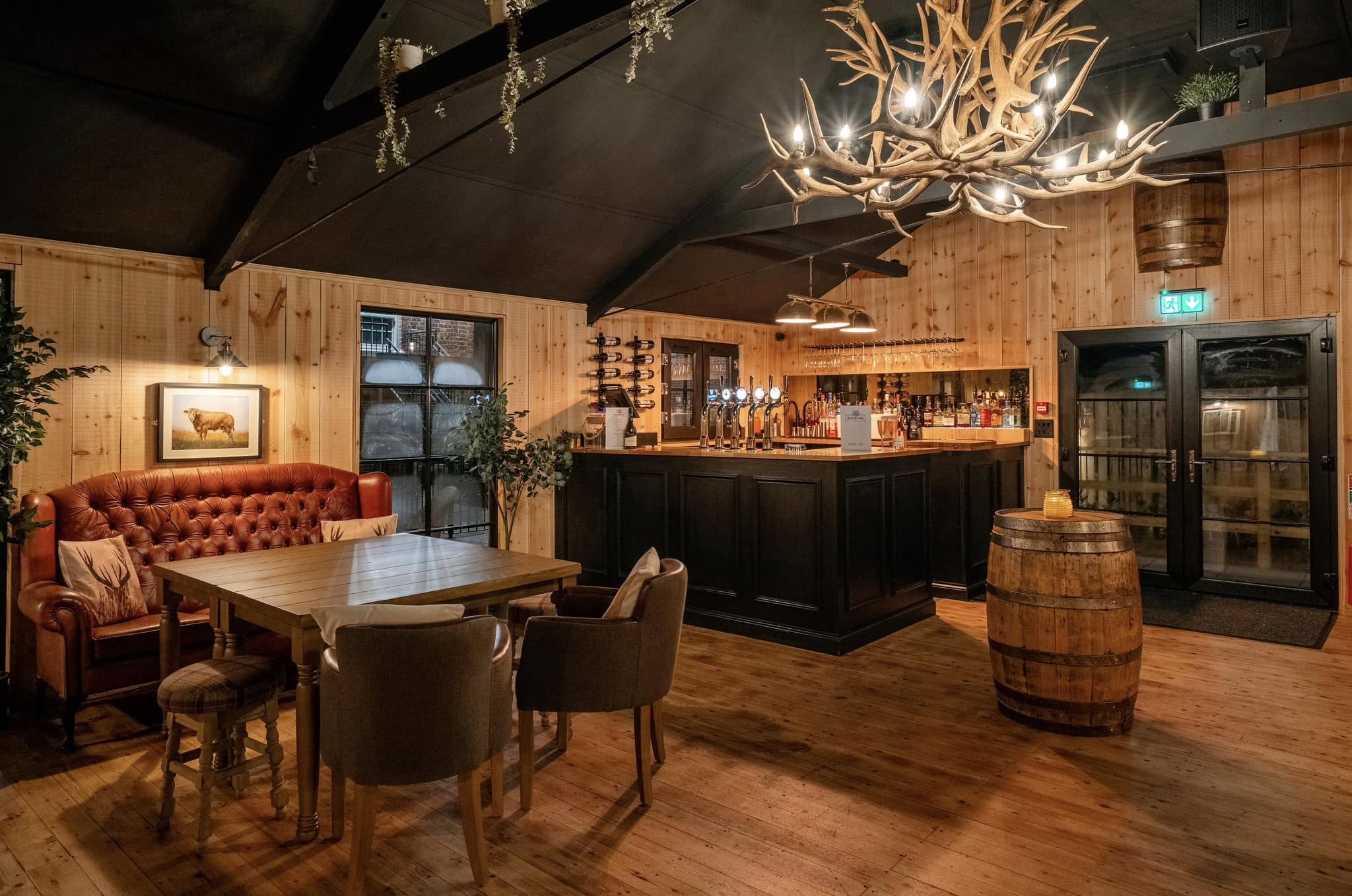 Wooden interior of a bar with rustic decor, including a chandelier and barrel.