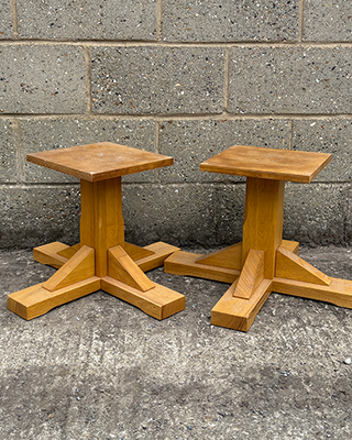 Two wooden stools with a star-shaped base against a concrete wall.