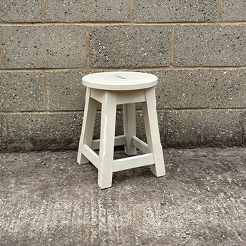 White stool against a gray brick wall on a concrete floor