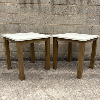 Two wooden tables with white tops against a concrete wall.