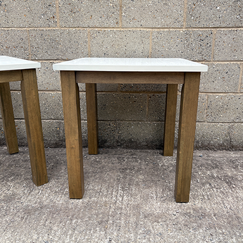Two wooden stools with white tops against a concrete wall.