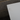 Close-up of a white rectangular object with small black specks on a dark textured surface