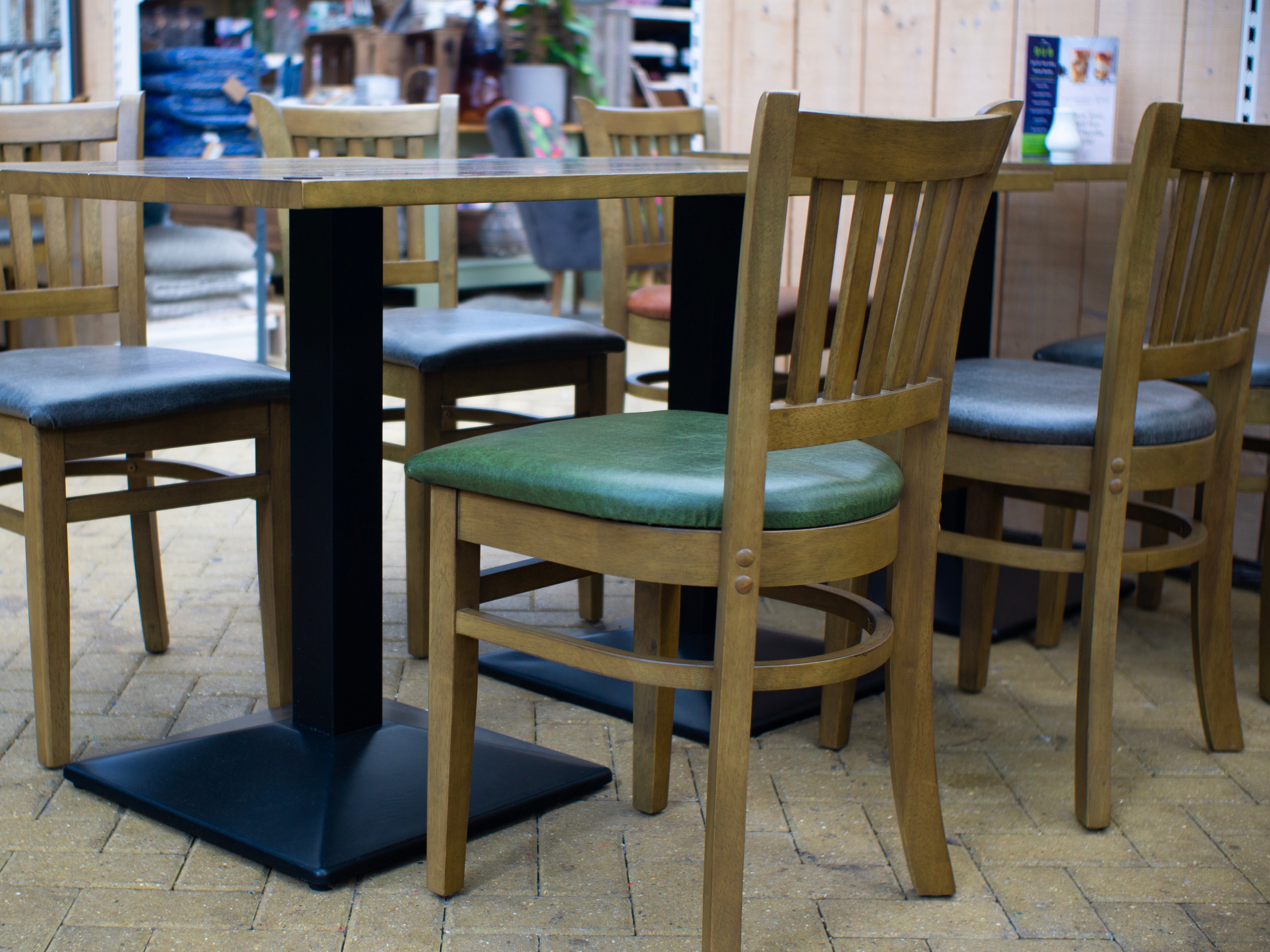 Wooden chairs with green cushions around a black metal table on a tiled floor.